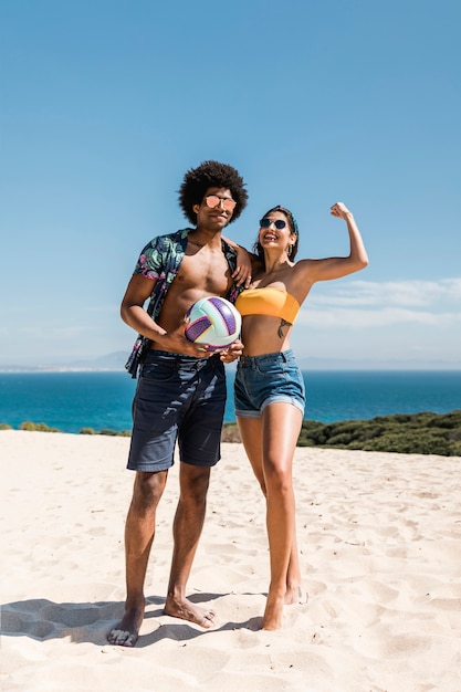 Couple multiracial avec ballon posant sur la plage