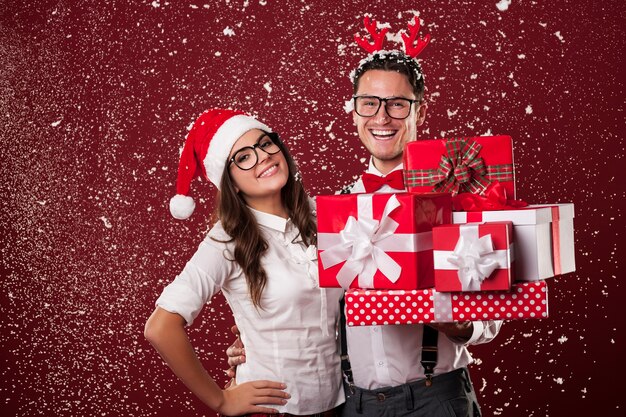 Couple de nerd souriant avec beaucoup de cadeaux de Noël pendant la neige