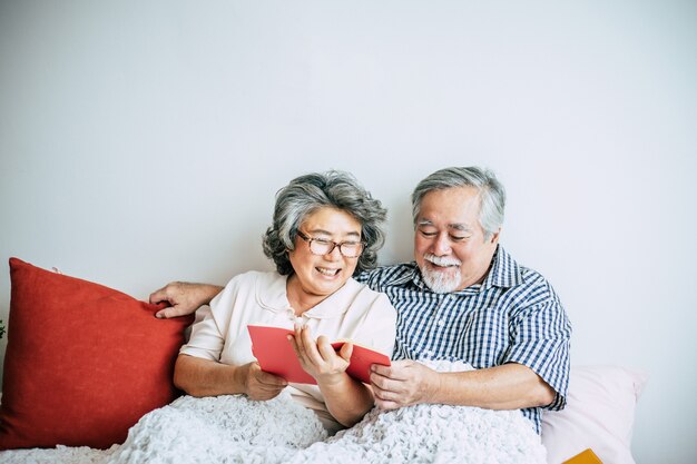 Couple de personnes âgées allongé sur le lit et lisant un livre