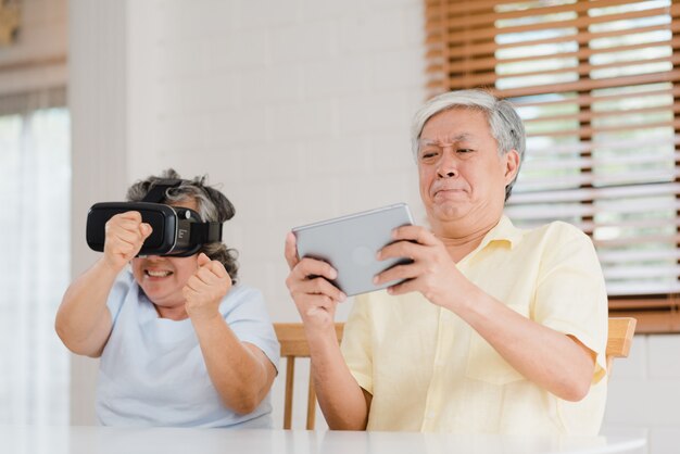 Couple de personnes âgées asiatique à l&#39;aide d&#39;une tablette et d&#39;un simulateur de réalité virtuelle jouant à des jeux dans le salon