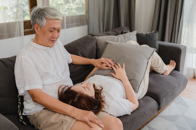 Couple de personnes âgées asiatique se détendre à la maison. Asiatiques grands-parents chinois, mari heureux sourire câlin allongez-vous sur ses genoux en position couchée sur le canapé dans le salon à la maison concept.
