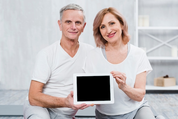 Couple de personnes âgées en bonne santé, regardant la caméra tenant une tablette numérique avec écran noir