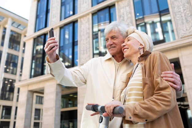 Couple de personnes âgées chevauchant un scooter électrique dans la ville et prenant un selfie