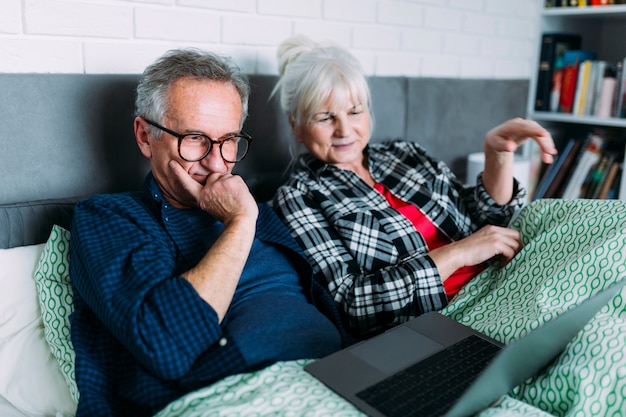 Couple de personnes âgées dans son lit en regardant un ordinateur portable