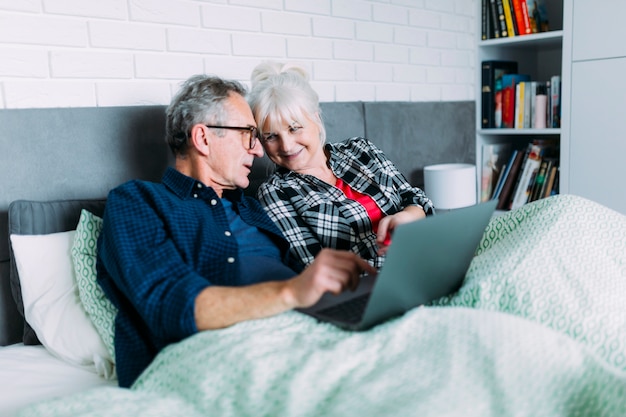 Photo gratuite couple de personnes âgées ensemble au lit avec un ordinateur portable