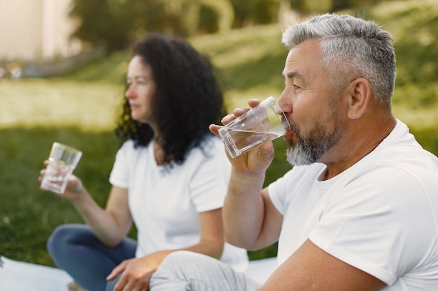 Photo gratuite couple de personnes âgées fait du yoga à l'extérieur. s'étendant dans le parc pendant le lever du soleil. brunette dans un t-shirt blanc.