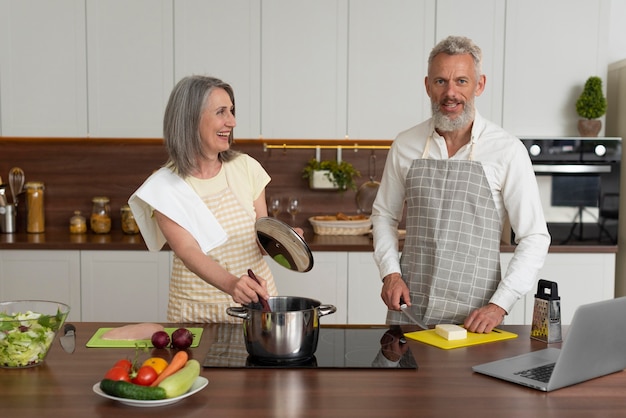 Couple de personnes âgées à la maison dans la cuisine prenant des cours de cuisine sur ordinateur portable