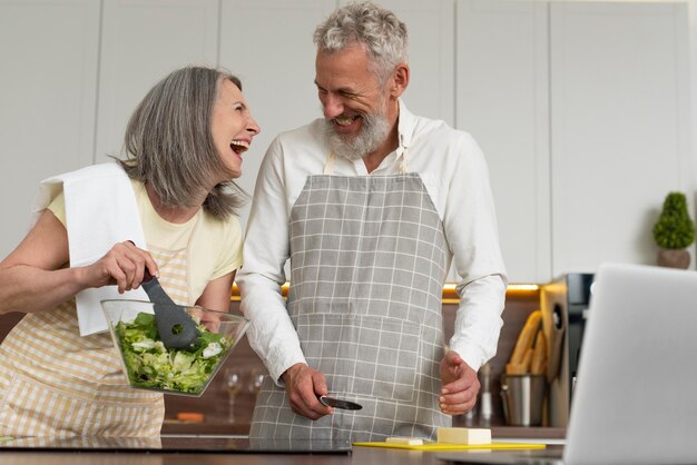 Couple de personnes âgées à la maison dans la cuisine prenant des cours de cuisine sur ordinateur portable