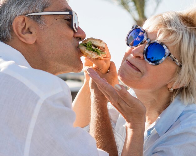 Couple de personnes âgées partageant un hamburger à l'extérieur