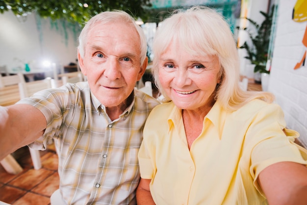 Photo gratuite couple de personnes âgées ravi assis dans un café et tir selfie