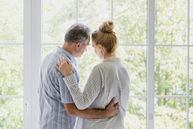 Couple de personnes âgées regardant ensemble par la fenêtre