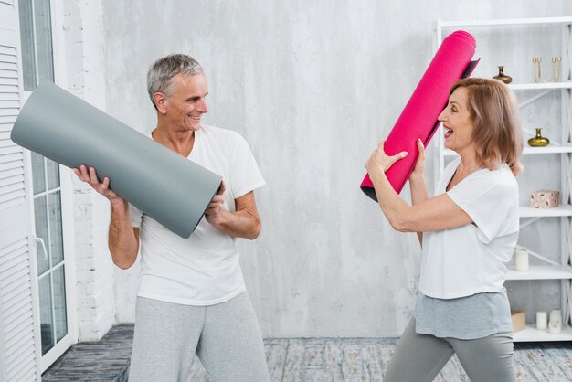 Couple de personnes âgées se battre avec tapis de yoga roulés à la maison