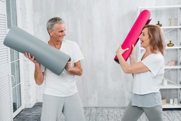 Couple de personnes âgées se battre avec tapis de yoga roulés à la maison