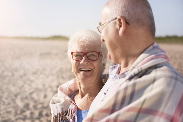 Couple de personnes âgées se réchauffant sous la couverture à la plage