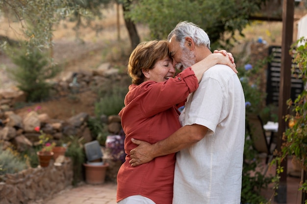 Couple de personnes âgées se tenant romantiquement dans leur jardin de campagne