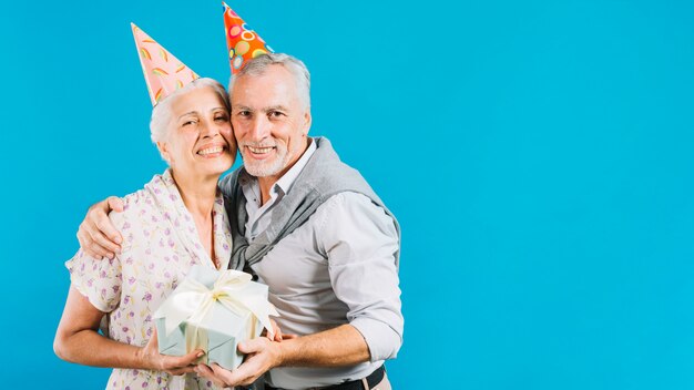 Couple de personnes âgées tenant un cadeau d&#39;anniversaire sur fond bleu