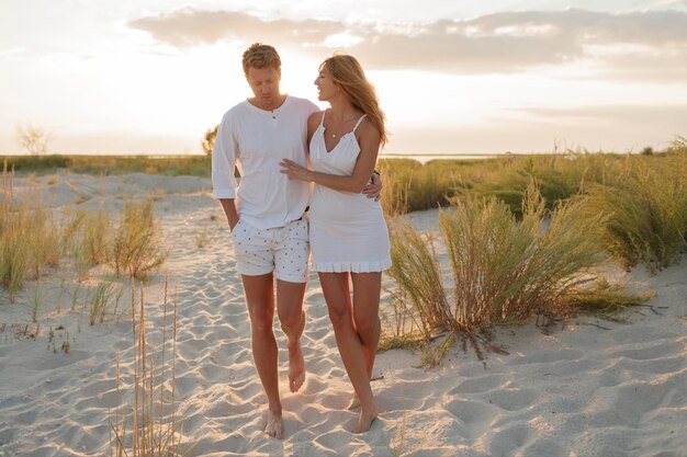 Couple de plage marchant pieds nus sur le sable au coucher du soleil à pied lune de miel.