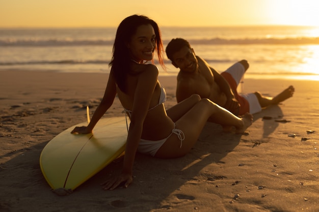 Couple avec planche de surf relaxant sur la plage au crépuscule