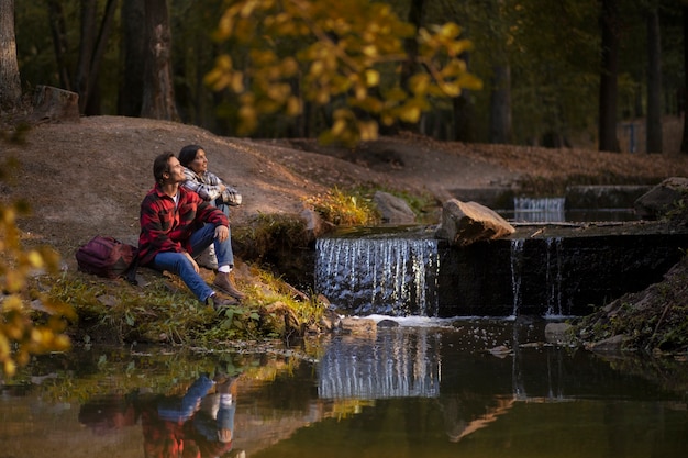 Photo gratuite couple plein coup assis au bord de la rivière