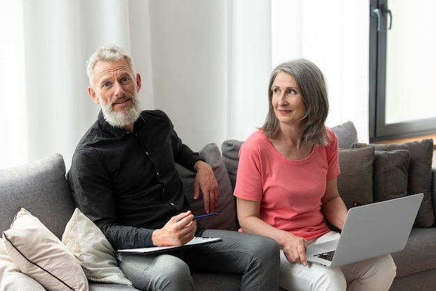 Couple plus âgé à la maison sur le canapé à l'aide d'un ordinateur portable