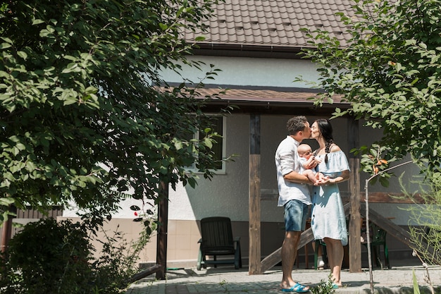 Couple portant leur bébé s&#39;embrasser devant la maison