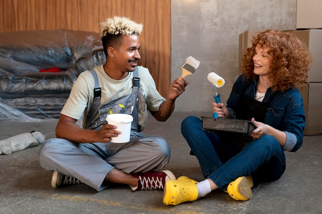 Couple posant ensemble dans leur nouvelle maison tout en tenant un pinceau