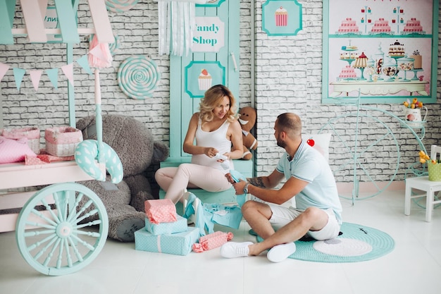 Couple de positivité de bel homme et jolie femme enceinte blonde assis dans les escaliers au studio embrassant l'estomac et gesticulant le cœur par les mains Jeune famille élégante à l'intérieur de la menthe douce parmi les jouets