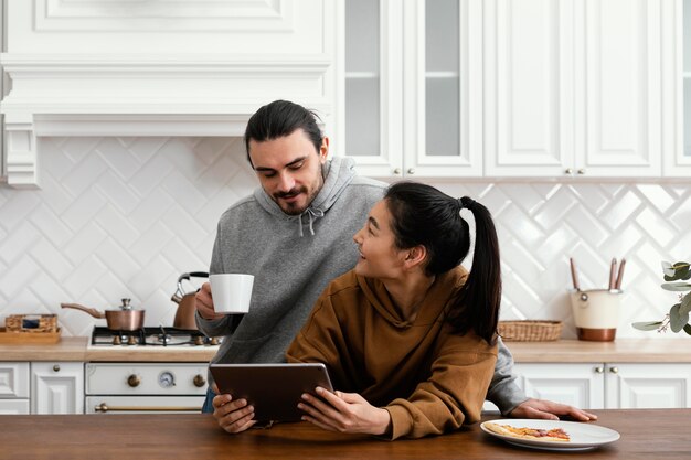 Couple prenant le petit déjeuner dans la cuisine et à l'aide d'une tablette