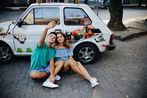 Couple prenant selfie assis contre voiture