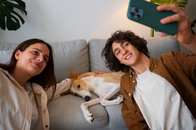 Photo gratuite couple prenant un selfie à la maison avec leur chien lévrier