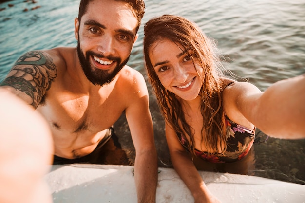 Couple prenant selfie en mer avec planche de surf