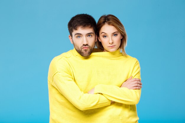 Couple en pull jaune posant avec les bras croisés sur le mur bleu