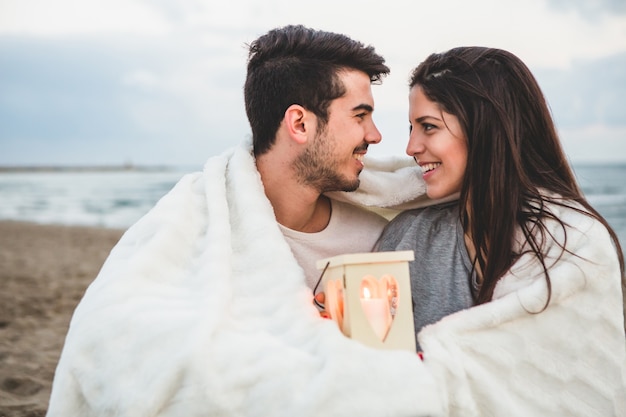 Couple regardant les uns les autres dans le sable avec une bougie et une couverture