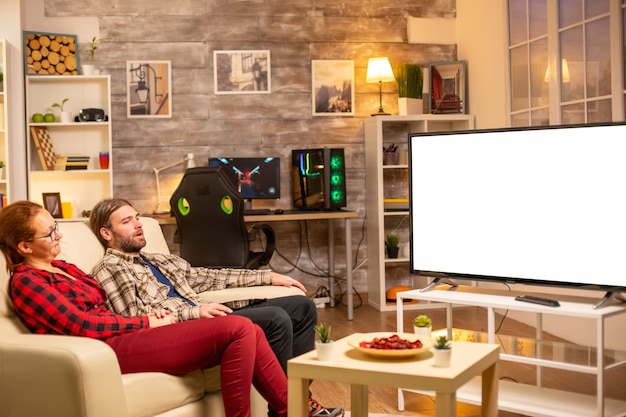 Couple regardant un écran de télévision blanc isolé tard dans la nuit dans le salon.