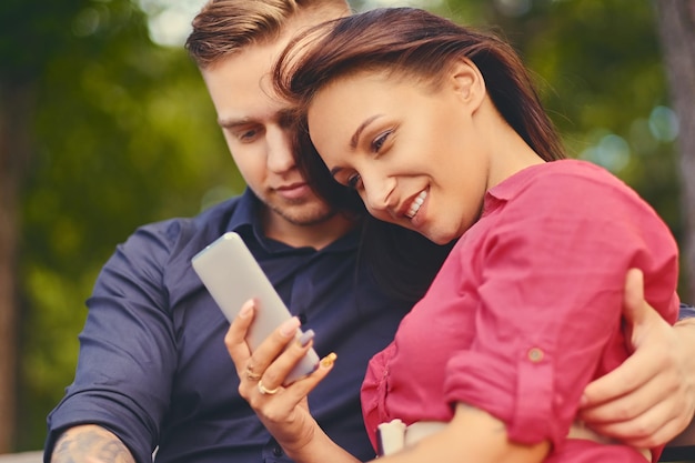 Un couple à un rendez-vous dans un parc de la ville à l'aide d'un smartphone et d'une messagerie instantanée.