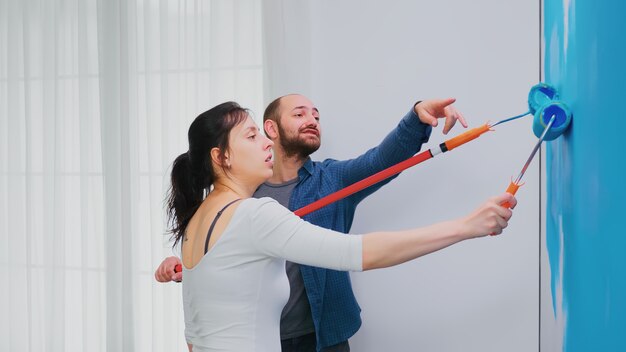 Couple repeint le mur de l'appartement avec de la peinture bleue à l'aide d'une brosse à rouleau. Redécoration d'appartements et construction de maisons tout en rénovant et en améliorant. Réparation et décoration.