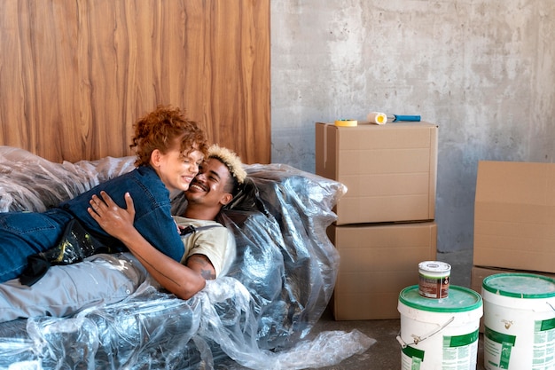 Couple reposant sur un canapé dans leur nouvelle maison à côté de seaux de peinture