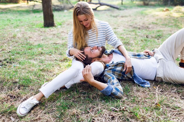 Couple romantique étreignant et assis dans le parc, vêtu d'une chemise à carreaux. Jeune fille blonde avec son beau petit ami avec barbe profitant d'une journée ensoleillée.