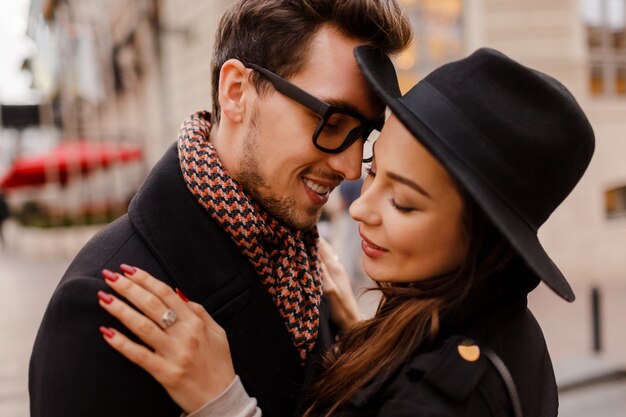 Couple romantique face à face étreignant et souriant. Couleurs chaudes et douillettes, ambiance hivernale. Bel homme et élégante femme aux cheveux noirs marchant dans la ville.