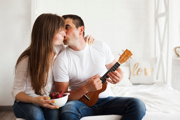 Couple romantique s'embrasser en jouant du ukulélé dans la chambre