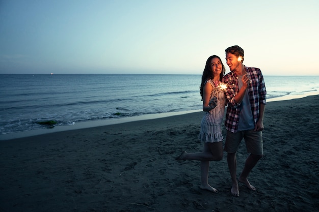 Couple romantique avec un sparkler à une plage du coucher du soleil