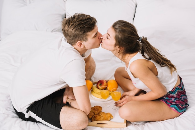 Couple s&#39;embrassant sur le lit avec plateau de nourriture