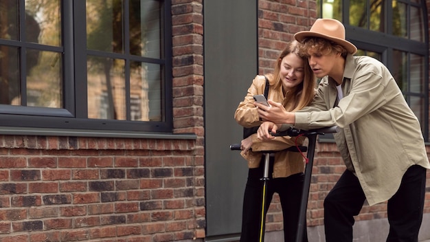 Photo gratuite couple avec scooters électriques et smartphone à l'extérieur