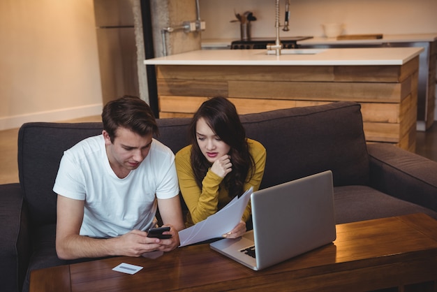 Couple Sitting On Sofa Discutant Avec Des Documents Financiers Dans La Salle De Séjour