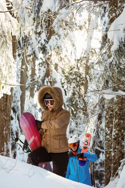 Couple avec ski et snowboard marchant sur la montagne enneigée