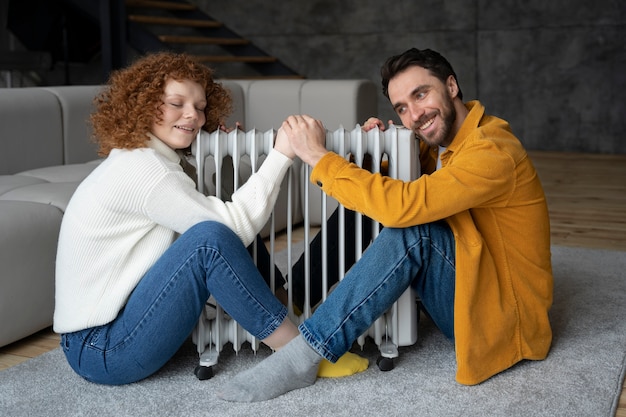 Couple de smiley plein coup se réchauffant avec un appareil de chauffage