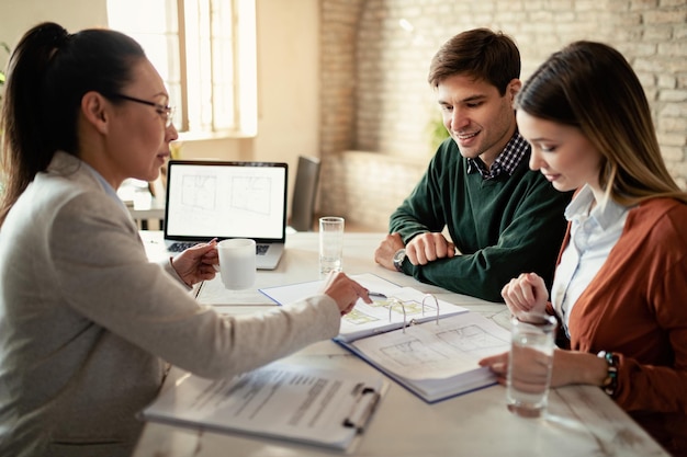 Photo gratuite couple souriant et agent d'assurance passant par des plans immobiliers lors d'une réunion au bureau l'accent est mis sur l'homme