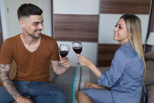 Couple souriant, assis sur le lit, grillage des verres à vin