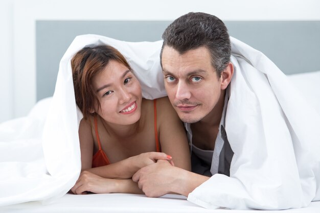 Couple souriant couvert de couverture au lit