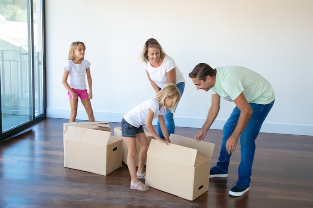 Couple souriant avec deux filles déballage des boîtes dans une salle vide